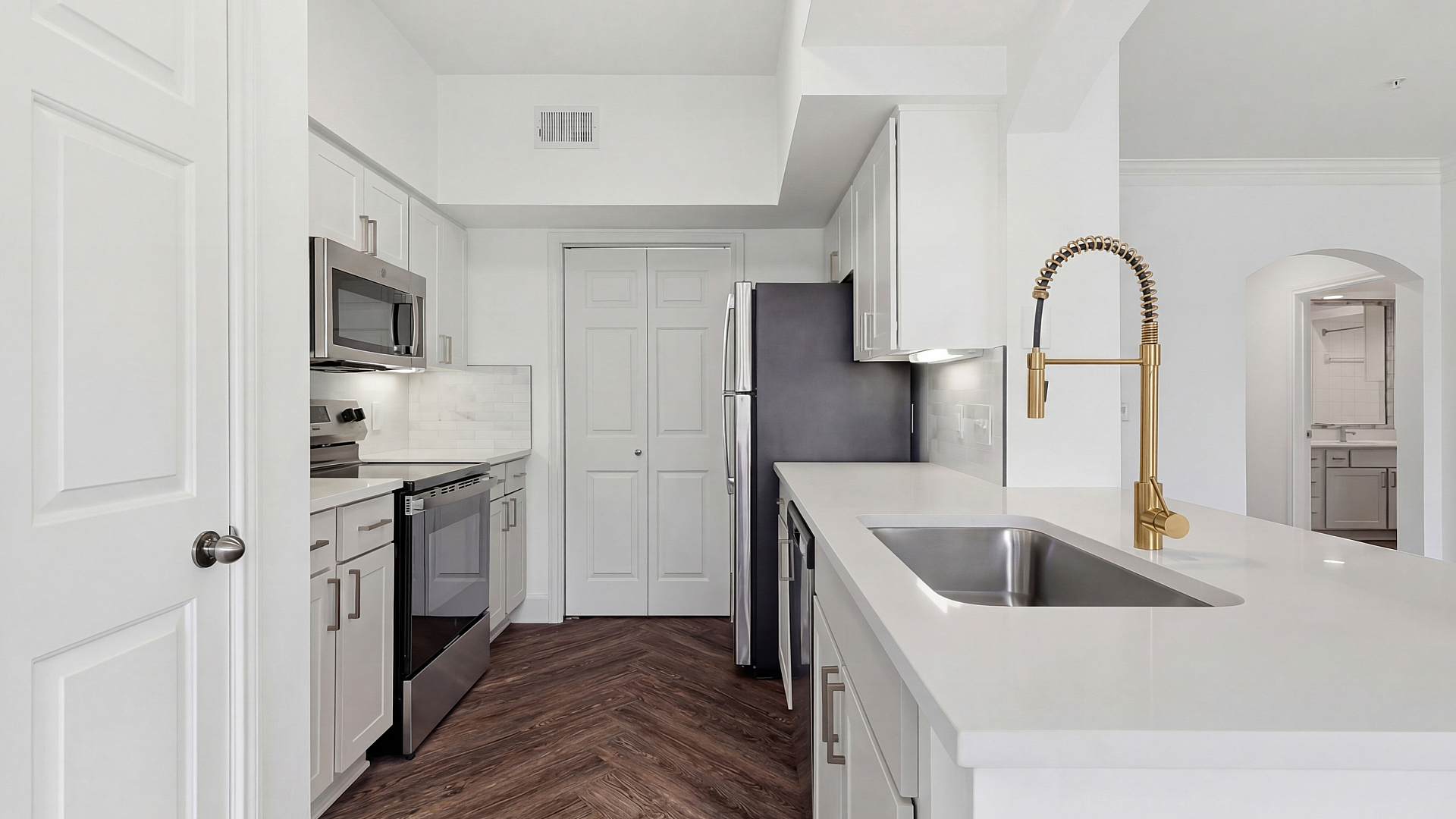 Modern kitchen with gleaming white countertops, sleek stainless steel appliances, and elegant wood flooring.