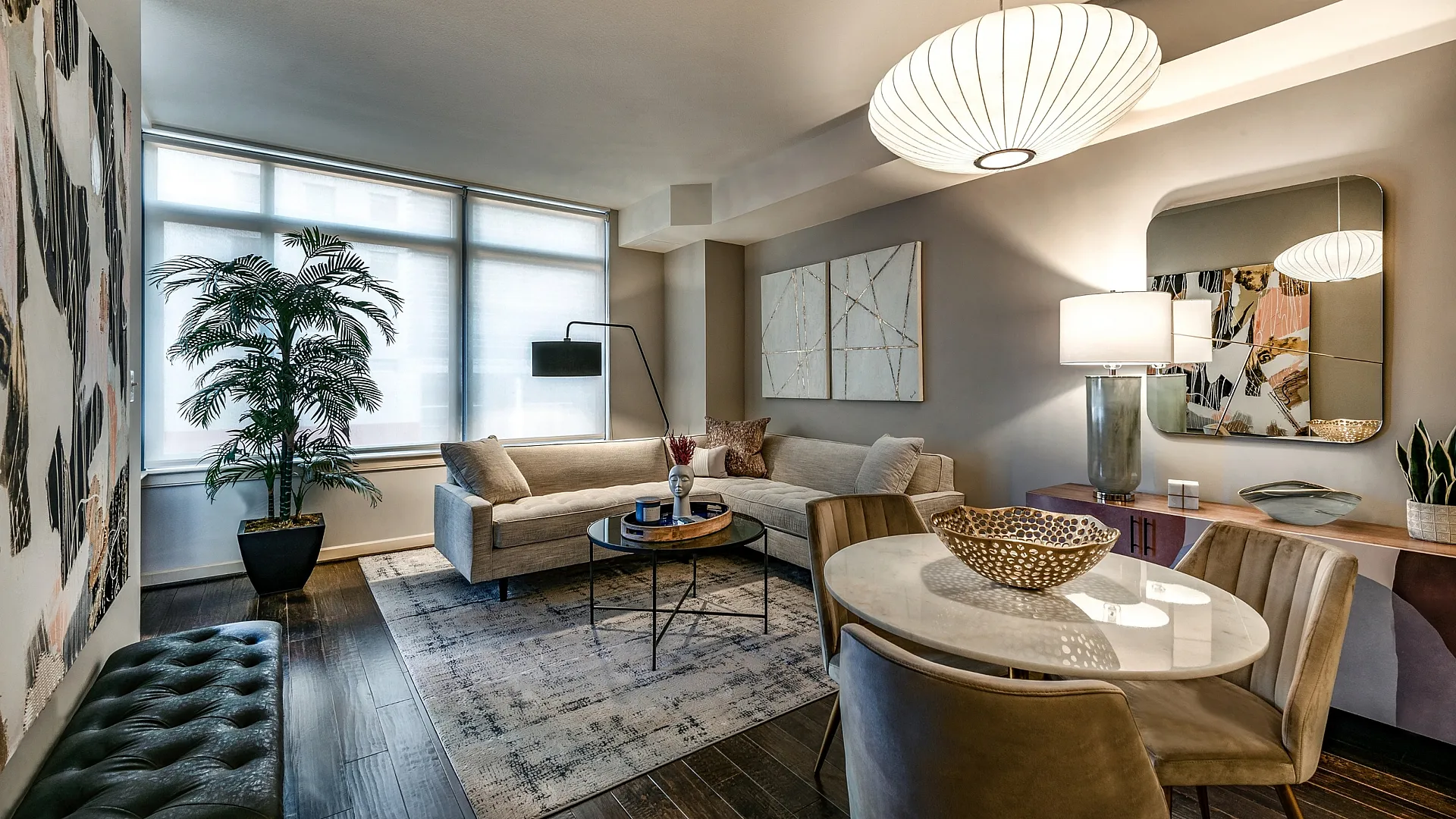 Elegant living room with modern decor, featuring a stylish beige sectional sofa, floor lamp, chic round table, and large windows offering natural light.