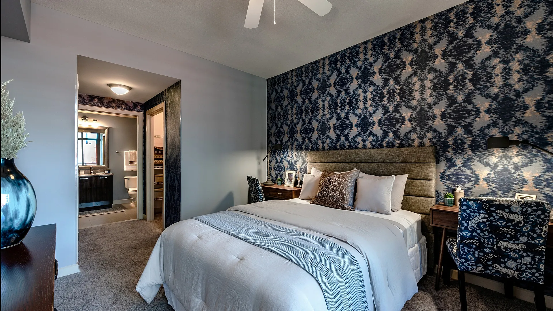 Elegant bedroom with luxurious bedding, stylish blue accent wall, and modern ensuite bathroom.