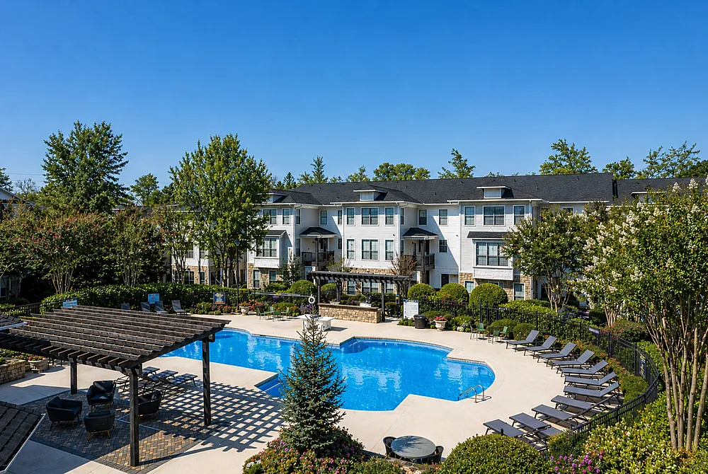 Charming apartment complex with a refreshing blue pool, surrounded by lush gardens and elegant seating under a stylish pergola.