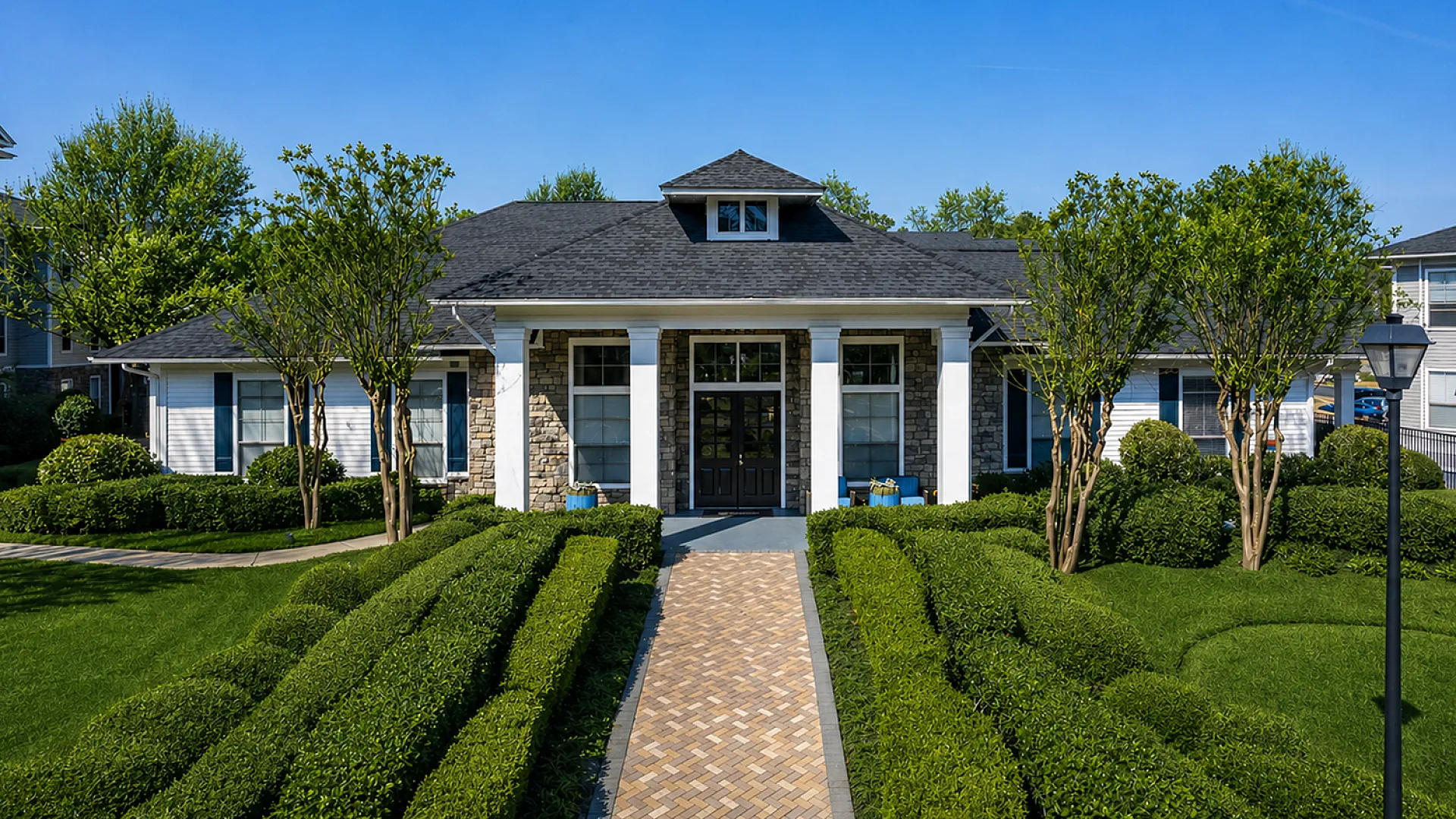 Elegant single-story home with a stone facade, welcoming entrance, manicured hedges, and lush green lawn under a bright blue sky.