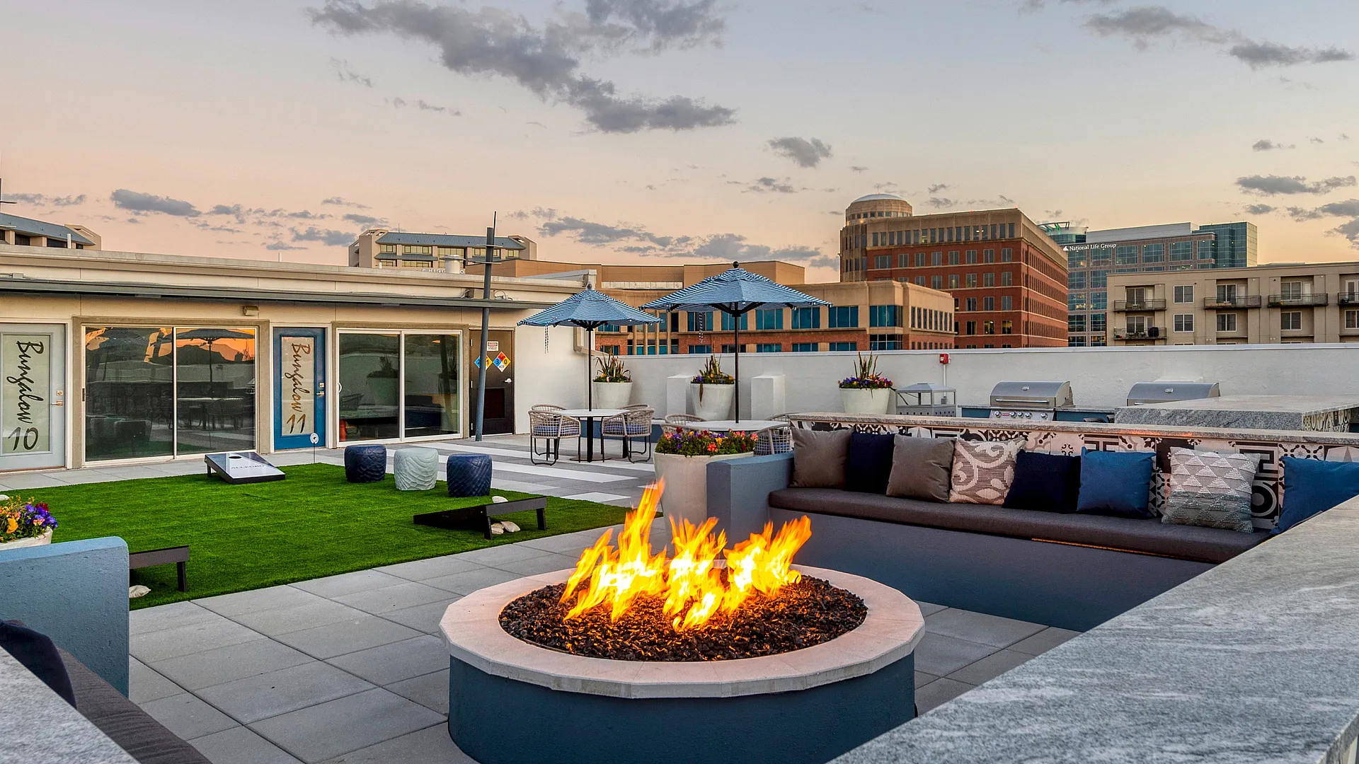 Chic rooftop patio with cozy fire pit, stylish seating, and stunning city skyline views at sunset.