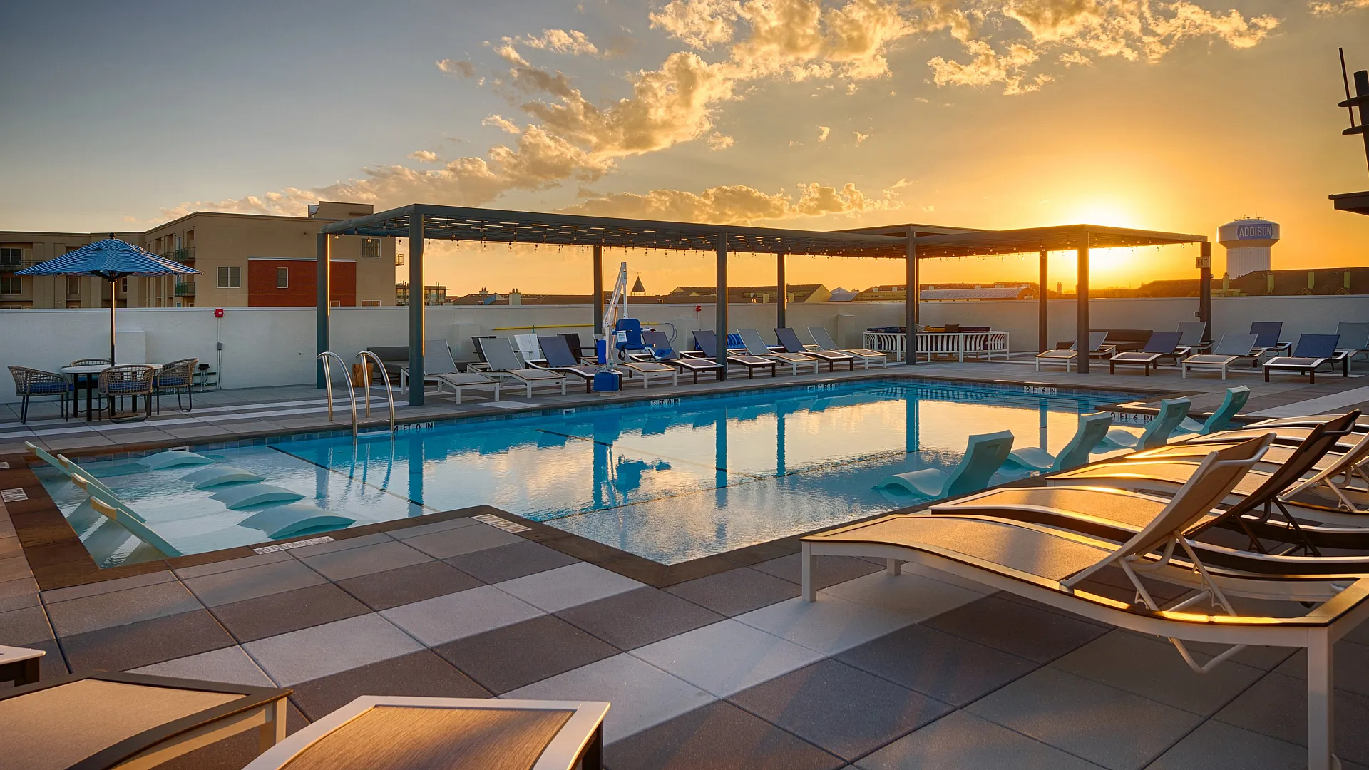 Chic rooftop pool area with elegant lounge chairs and stunning sunset views, perfect for relaxation.