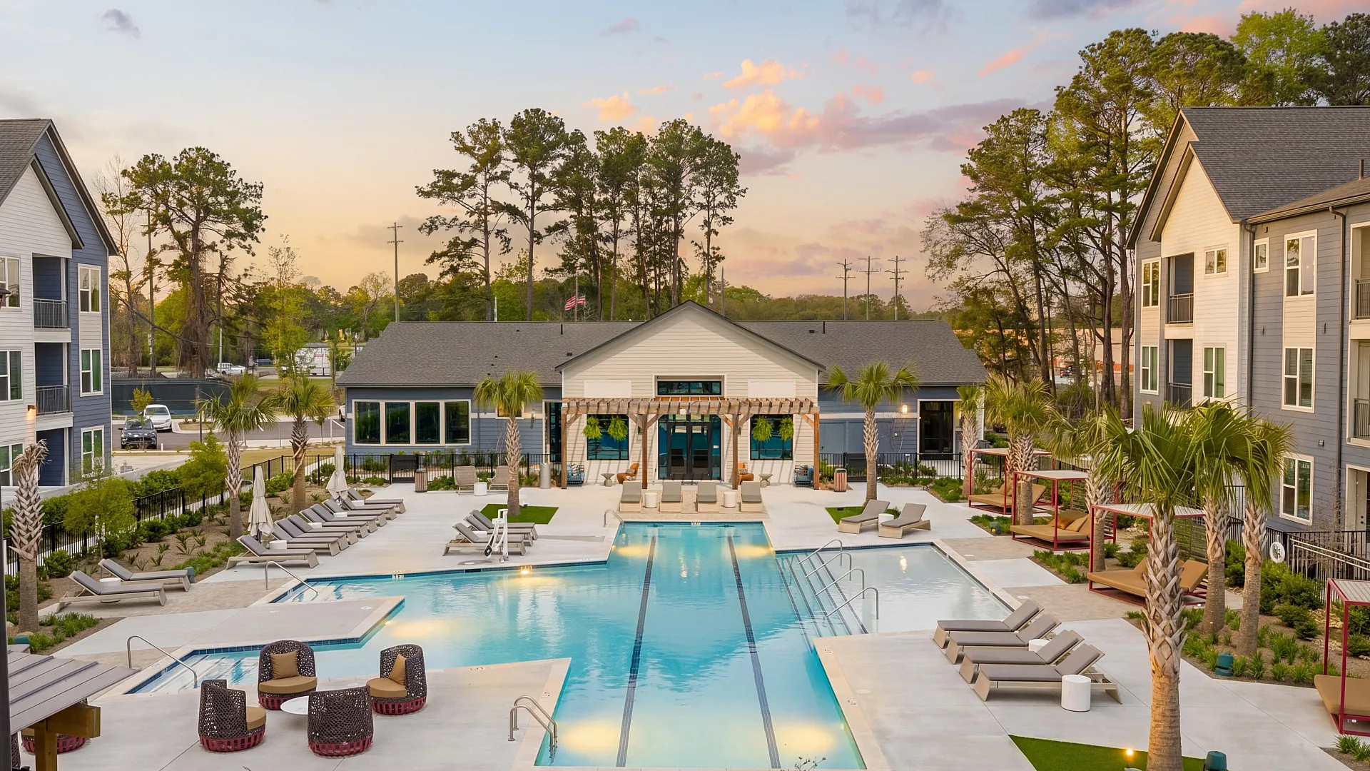 Vibrant apartment complex with spacious pool, modern lounge areas, and palm trees at sunset.