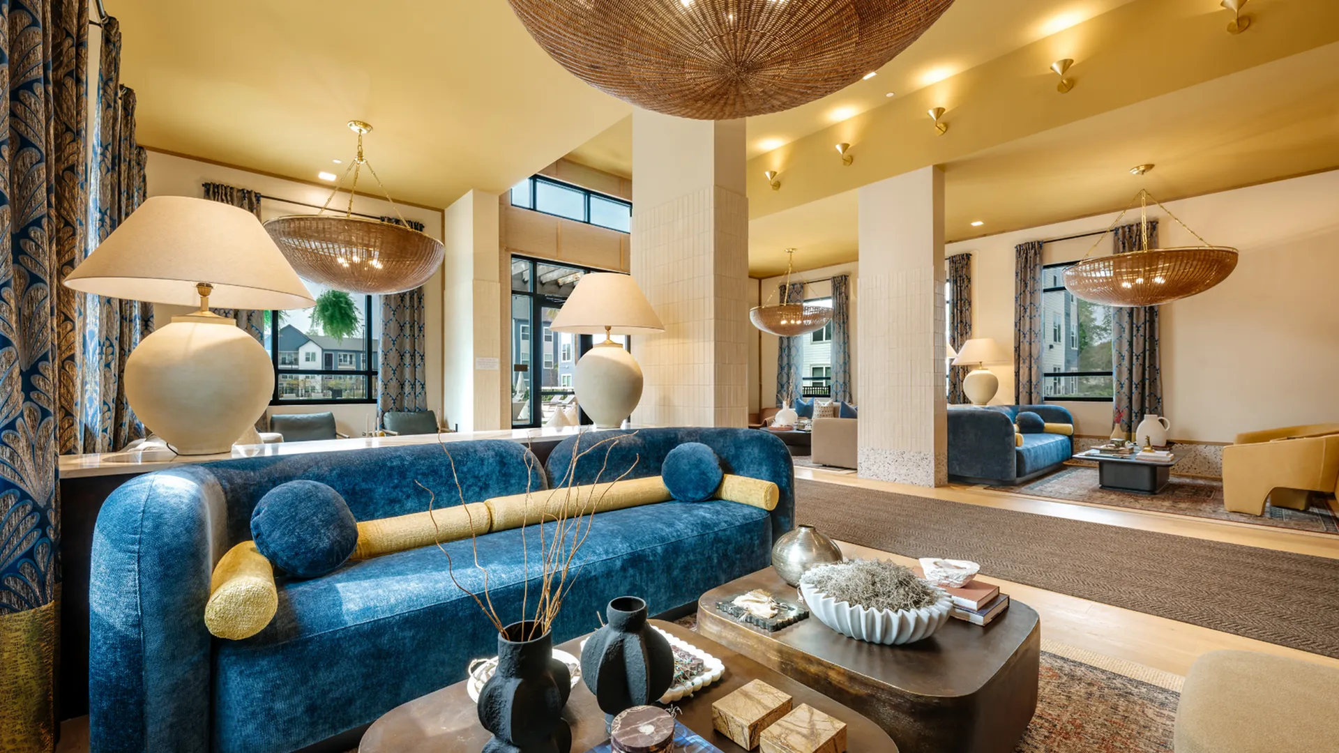 Luxurious apartment interior with elegant decor featuring plush blue sofas, stylish lamps, and chic artwork in a sunlit living area.