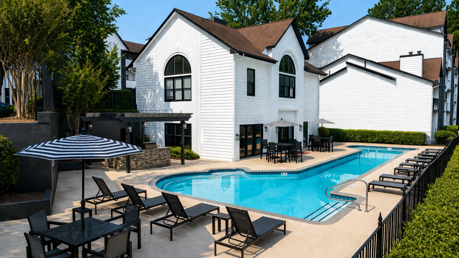Charming residential complex with a sparkling outdoor pool, stylish loungers, and modern patio furniture surrounded by lush greenery.
