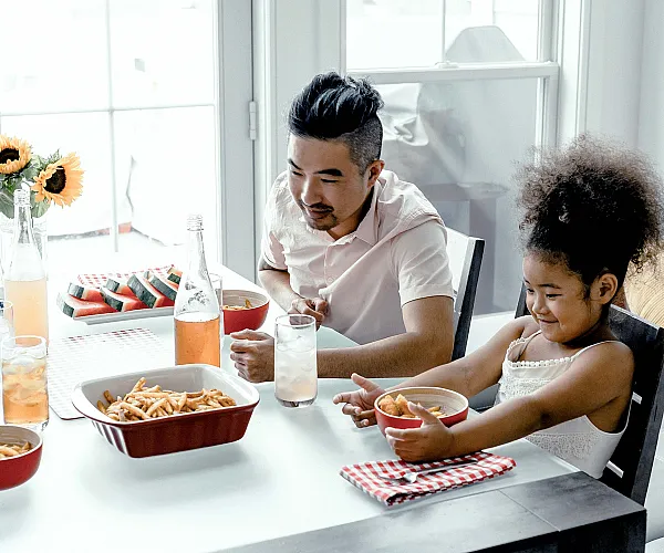 Bright dining area with cheerful family enjoying a meal, featuring sunflowers, fresh watermelon, and stylish decor.