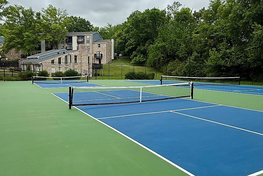 Inviting apartment complex with modern architecture, nestled behind vibrant tennis courts, surrounded by lush greenery.