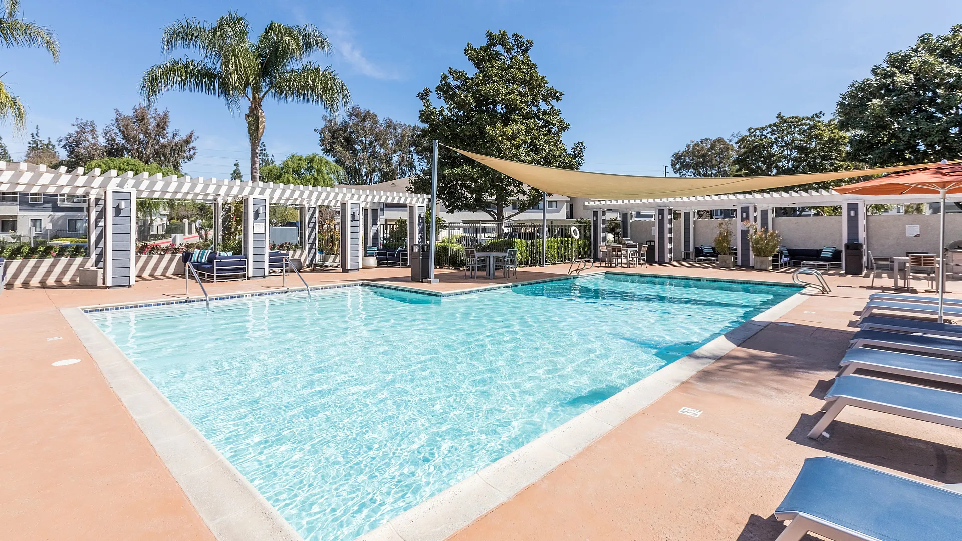 Inviting outdoor pool area with sun loungers, stylish pergolas, and lush palm trees, perfect for relaxation in a sunny setting.
