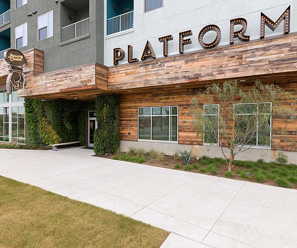 Modern apartment exterior with stylish wood accents, lush greenery, and bold 'PLATFORM' signage.