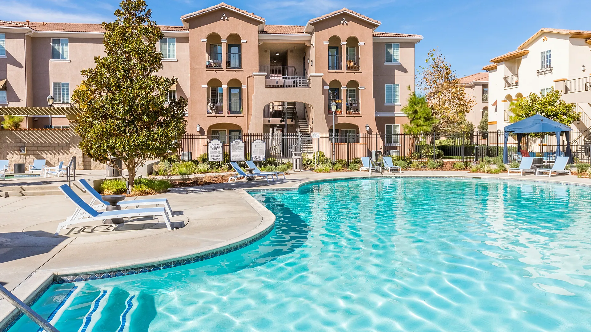 Sunny apartment complex with inviting pool and stylish lounge area, perfect for relaxation and leisure.