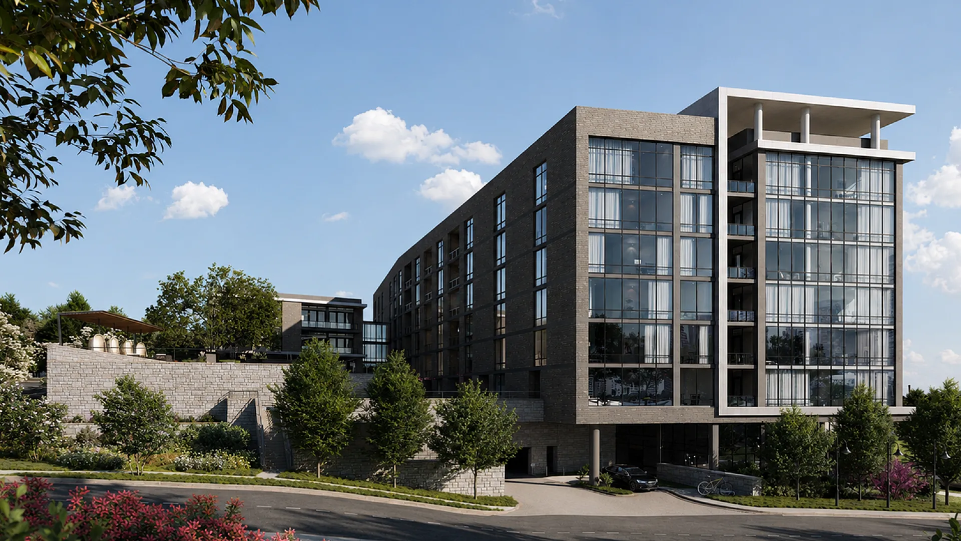 Luxurious modern apartment building with expansive glass windows, surrounded by lush greenery and a paved entrance, set against a clear blue sky.