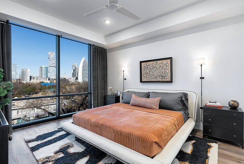 Luxurious bedroom with modern decor, featuring a plush bed and floor-to-ceiling windows offering stunning cityscape views.