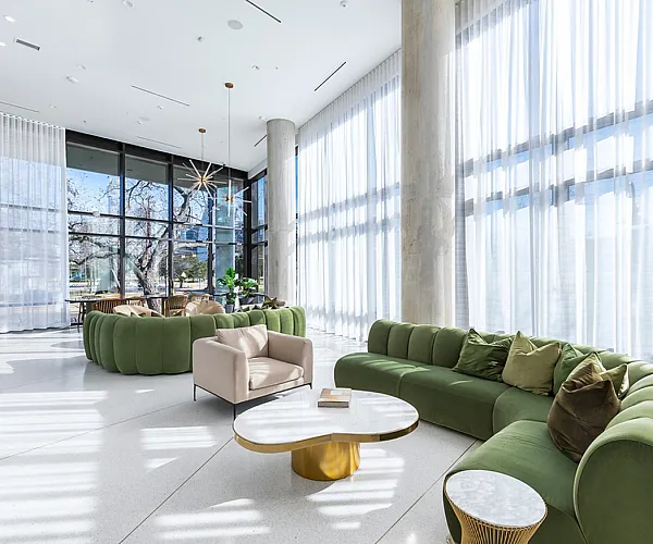 Elegant and spacious lounge with plush green sofas, floor-to-ceiling windows, and modern d&eacute;cor, inviting abundant natural light.