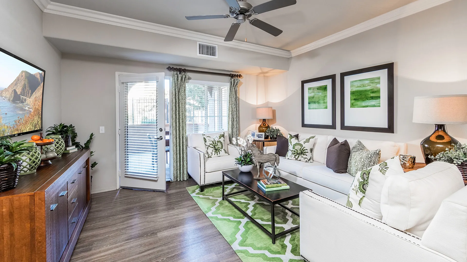 Bright and modern living room with elegant decor, featuring a plush white sofa, vibrant green rug, and stylish wooden furniture, enhanced by ample natural light from large windows.