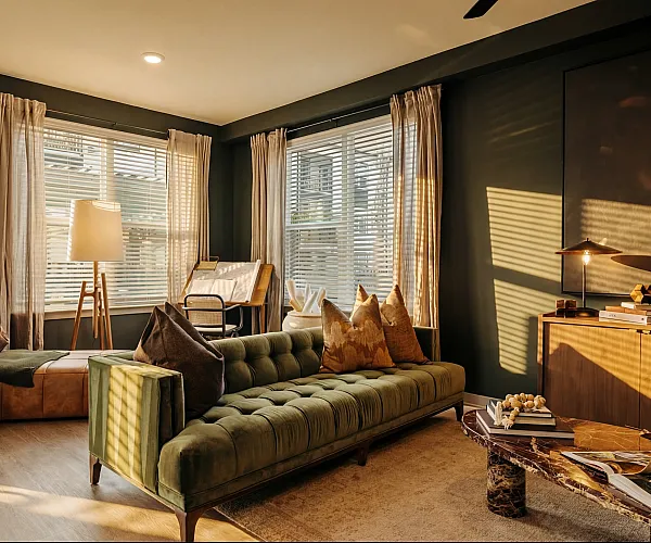 Inviting living room with mid-century modern decor, featuring a plush green velvet sofa, elegant wooden furnishings, and sunlight streaming through large windows.