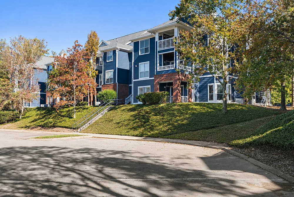 Charming blue apartment complex with spacious balconies, nestled in a lush green landscape surrounded by mature trees.