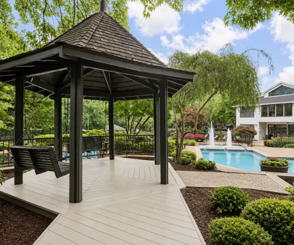 Charming outdoor space featuring a cozy gazebo next to a sparkling pool surrounded by lush greenery and a modern clubhouse.