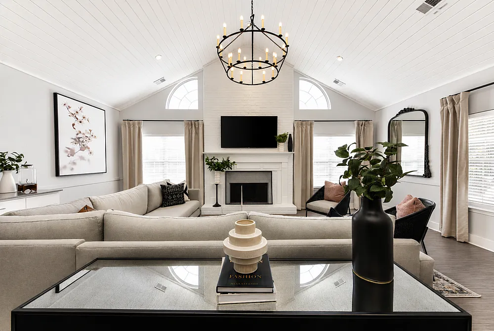 Elegant living room with a vaulted ceiling and chandelier, featuring a cozy fireplace, modern decor, and large windows for natural light.