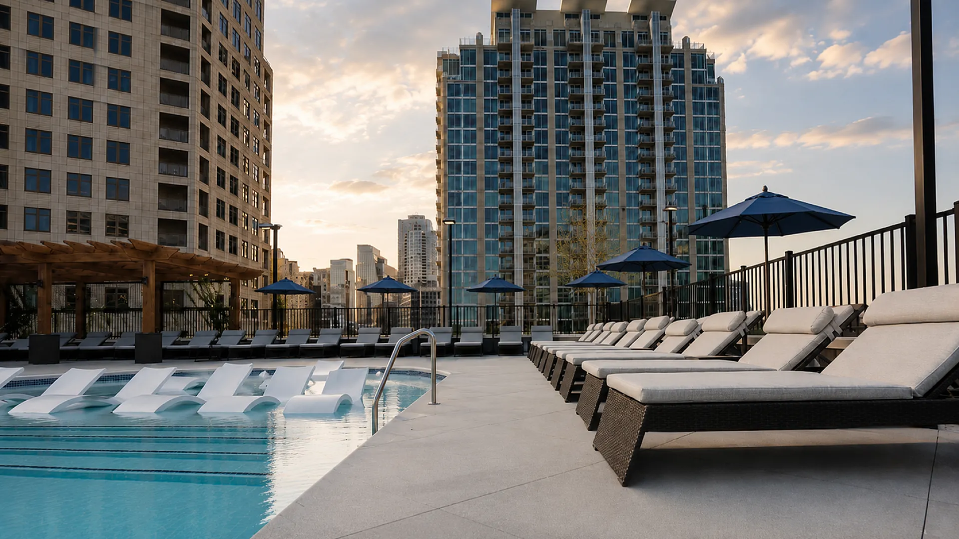 Luxurious rooftop pool area with stylish lounge chairs and a stunning cityscape backdrop at sunset, perfect for relaxation and leisure.
