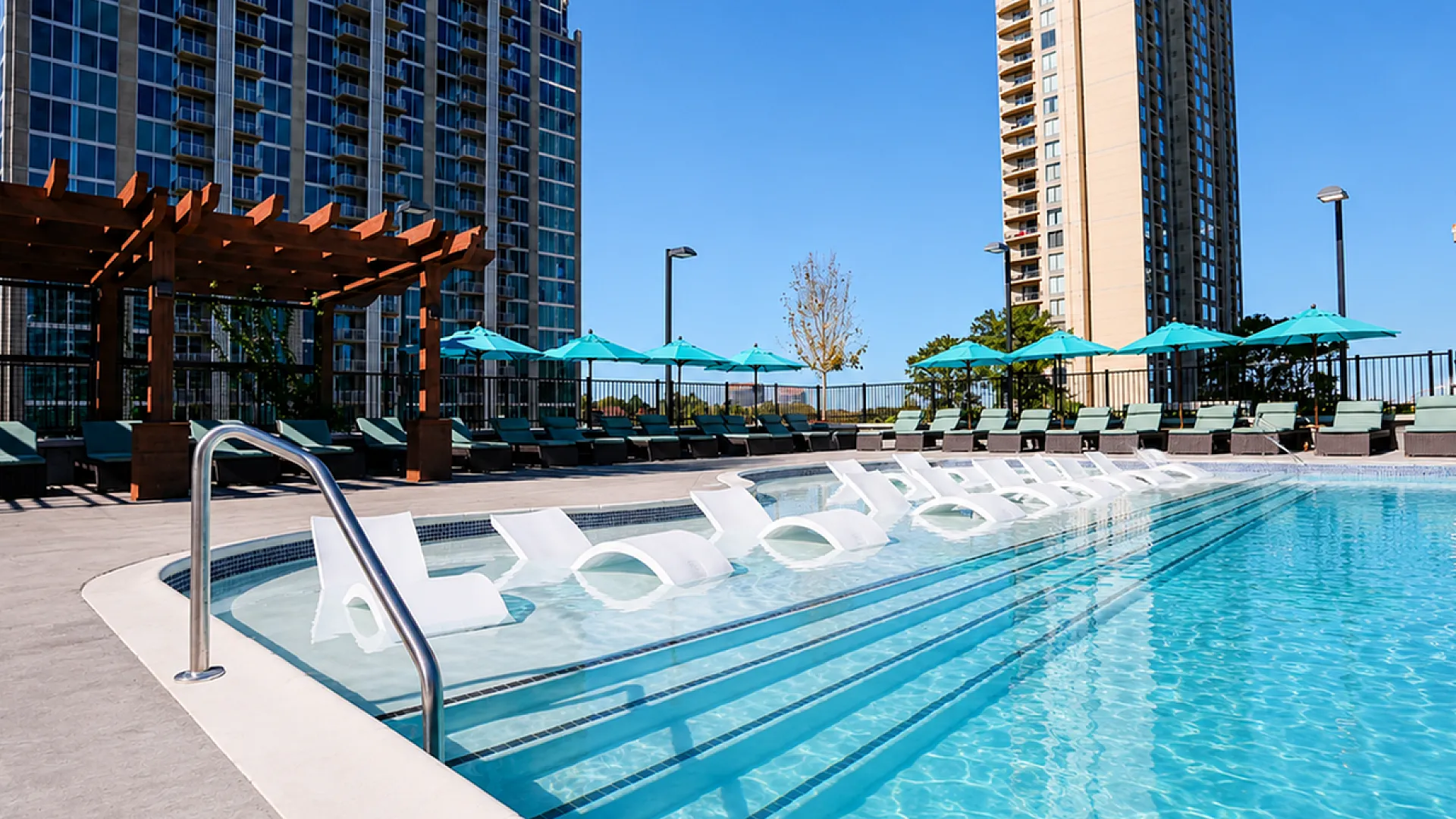 Luxurious outdoor pool area with modern lounge chairs, poolside seating, and stunning high-rise views, perfect for relaxation and enjoyment.