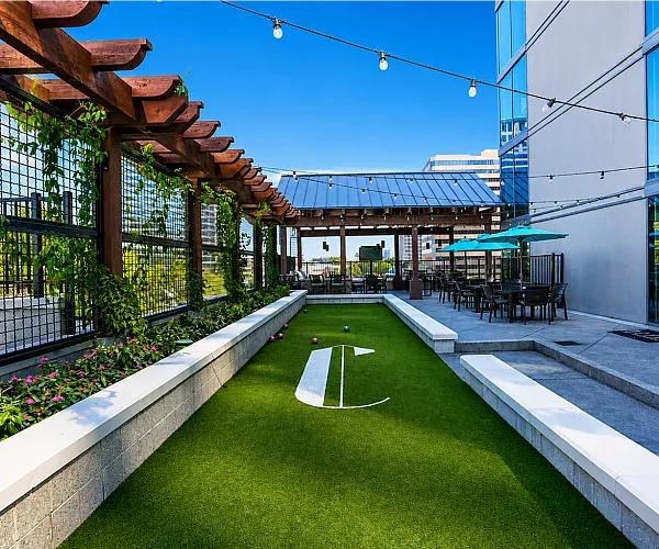 Luxurious rooftop terrace featuring a bocce court, elegant pergola, and stylish outdoor dining area with vibrant city views.