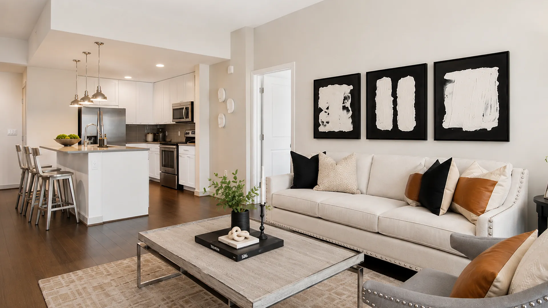 Modern open-plan living room and kitchen featuring sleek white cabinetry, elegant pendant lighting, and stylish d&eacute;cor.