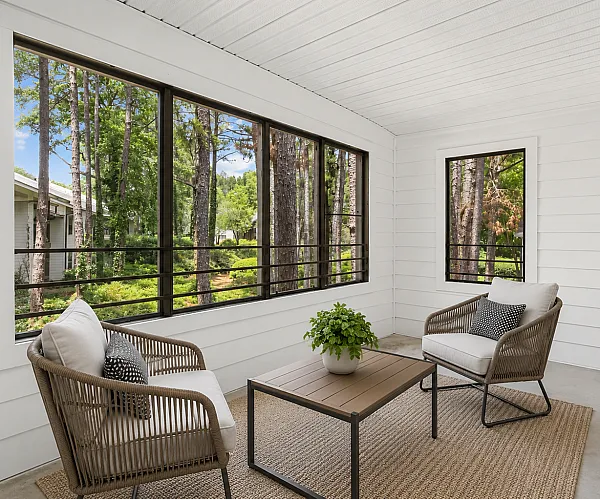 Charming sunroom with elegant wicker furniture and large windows overlooking a lush, serene wooded landscape.