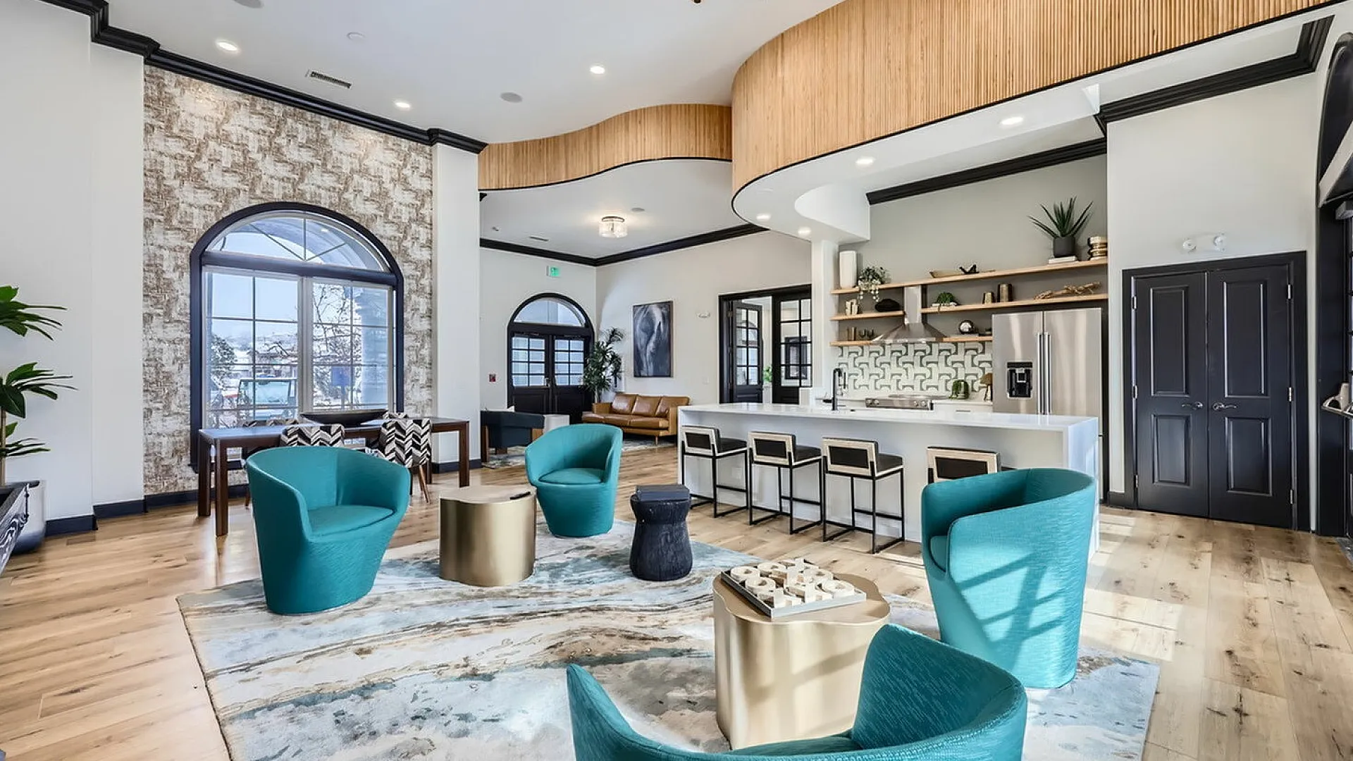 Luxurious and modern communal area featuring stylish teal seating, chic bar stools at a sleek white counter, and elegant wood accents in a bright, airy space.