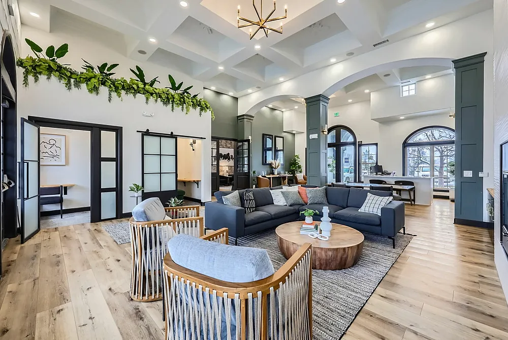 Elegant and modern living space featuring high ceilings, stylish seating area, and lush greenery. Warm wooden floors complement the chic decor.