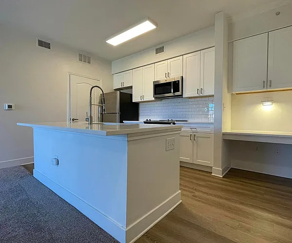 Modern kitchen with sleek white cabinetry, central island, elegant faucet, and cozy adjacent workspace in a stylish open-concept apartment.