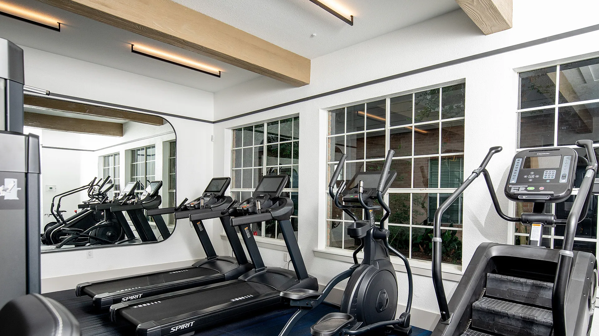 Modern fitness center equipped with state-of-the-art treadmills, elliptical, and a stair climber, surrounded by large windows for a bright and energizing workout atmosphere.