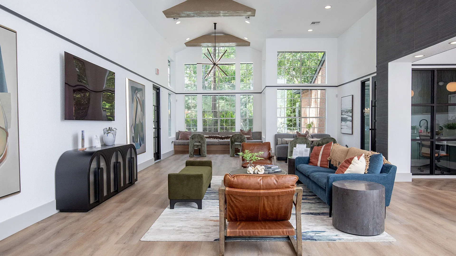 Bright and spacious modern living room with high ceilings, sleek wooden flooring, and large windows offering a scenic view of greenery.