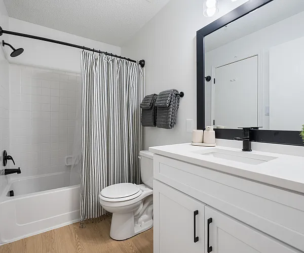 Elegant bathroom featuring a modern vanity with black accents, pristine bathtub with chic shower curtain, and stylish decor.