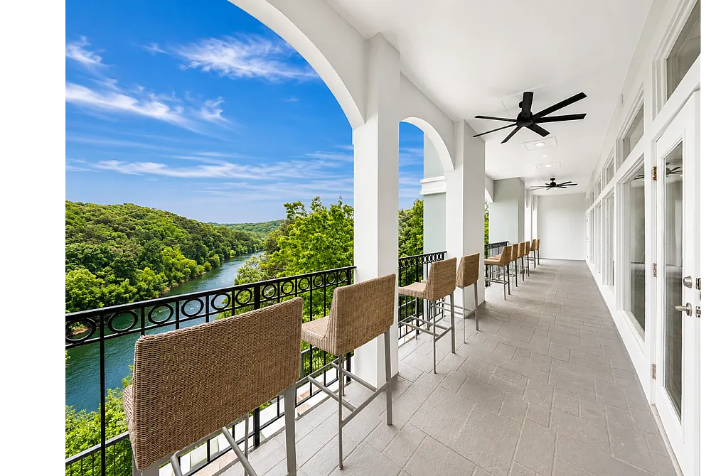 Luxurious apartment balcony with stylish seating, offering breathtaking river and lush green views under a clear blue sky.