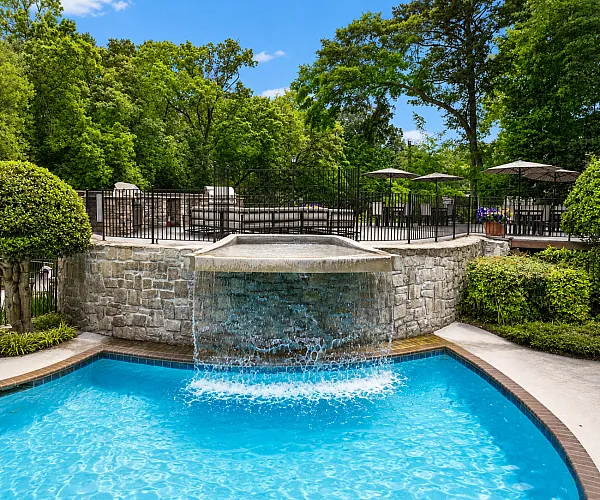 Luxurious outdoor pool area featuring a cascading waterfall, lush green landscaping, and elegant seating with umbrellas.