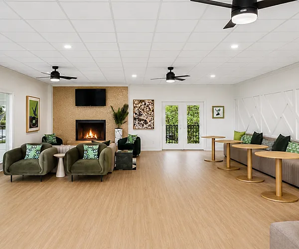 Spacious and inviting lounge area with modern decor, cozy green armchairs, and elegant wood flooring. Features large windows for natural light and a stylish fireplace centerpiece.