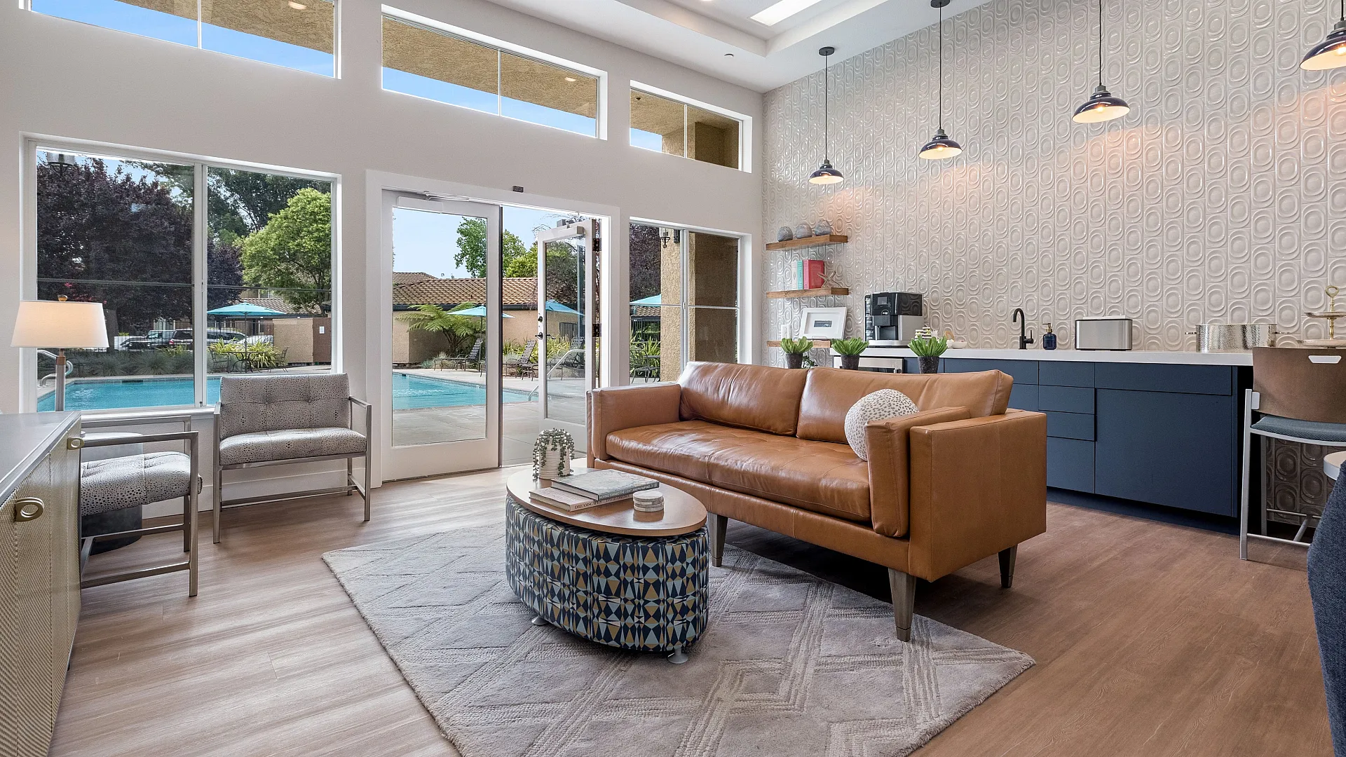 Chic living room with modern decor, sleek leather sofa, and large windows overlooking a sparkling pool.