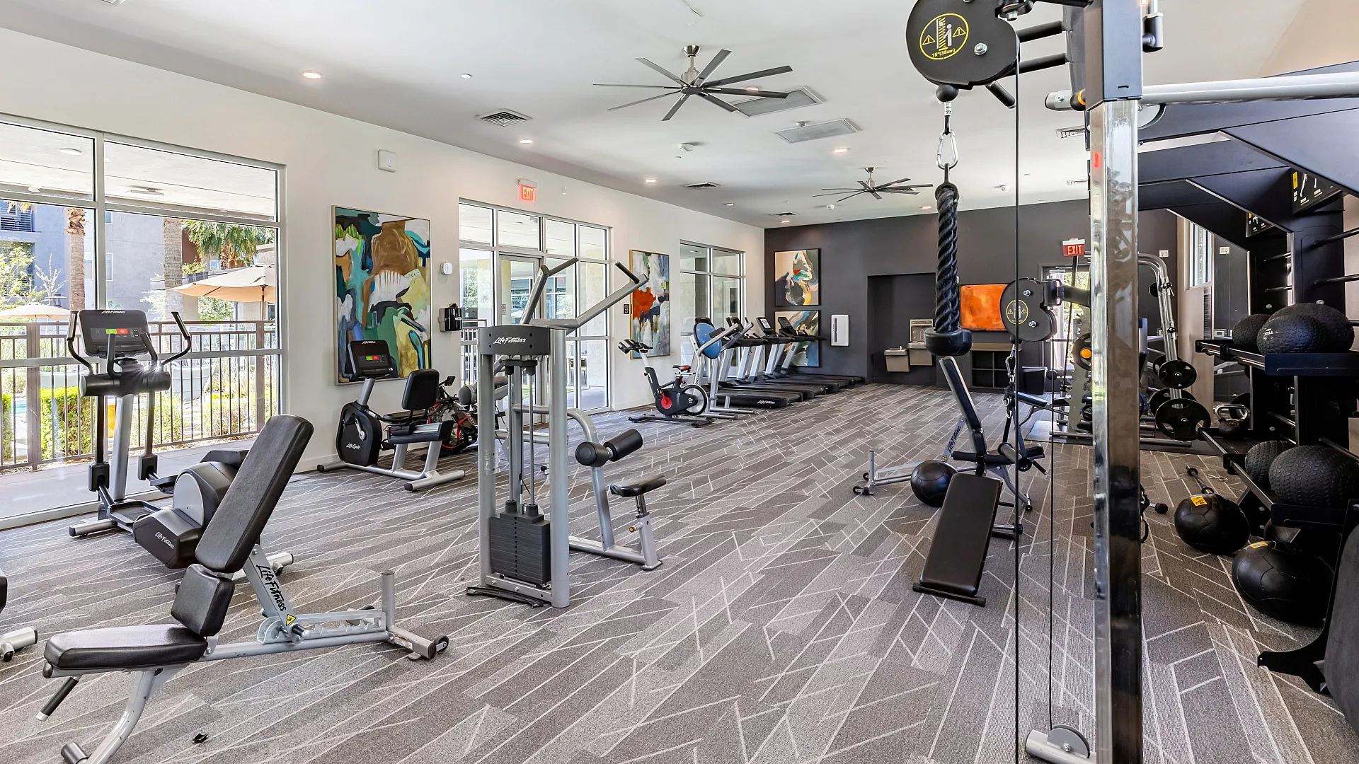 Modern fitness center featuring state-of-the-art exercise equipment, expansive windows, and vibrant artwork for an invigorating workout experience.