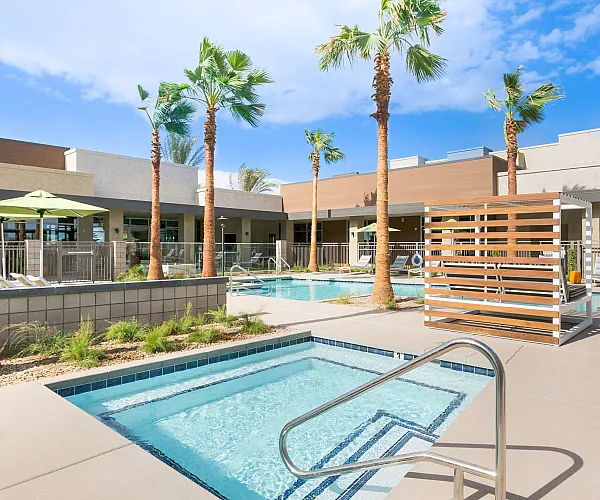 Relaxing outdoor pool area with palm trees, modern lounges, and a sparkling hot tub under a bright blue sky.