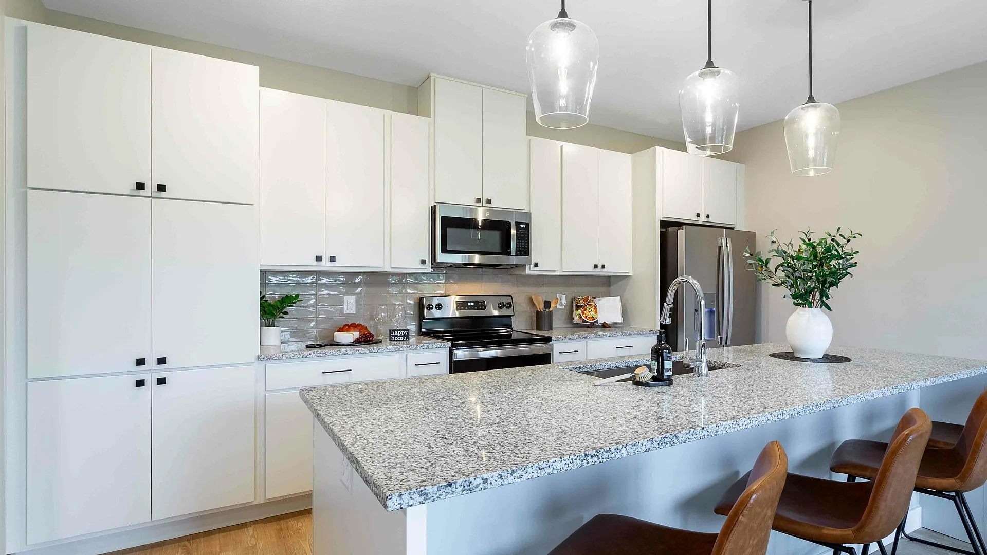 Modern kitchen with sleek granite countertops, elegant cabinetry, and stylish pendant lighting over a spacious island with leather barstools.