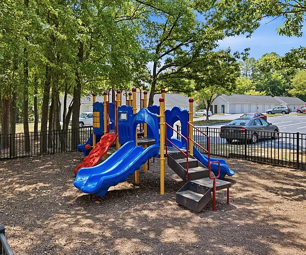 Inviting playground with vibrant blue and red slides, surrounded by lush trees, ideal for family fun and relaxation.