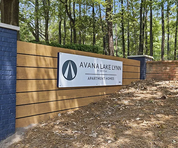 Inviting entrance to Avana Lake Lynn Apartment Homes, featuring a stylish sign set against a backdrop of lush trees and a well-maintained landscape.