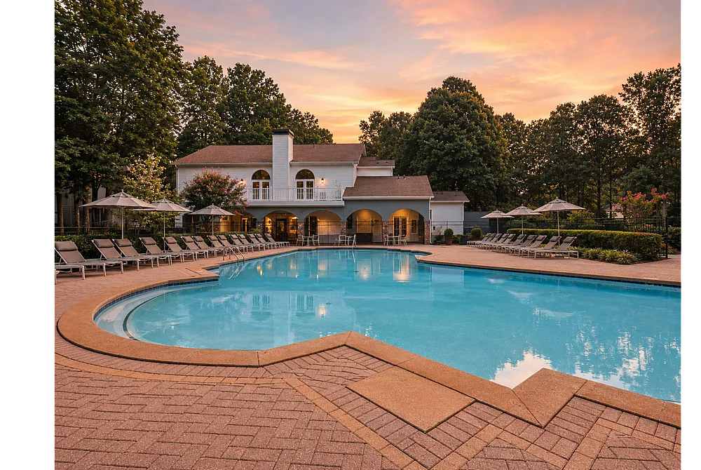 Beautiful outdoor pool area with elegant loungers and a scenic view of a luxurious clubhouse against a sunset sky.