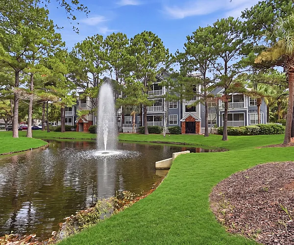Charming apartment exterior nestled amidst lush greenery and serene pond with a striking central fountain.
