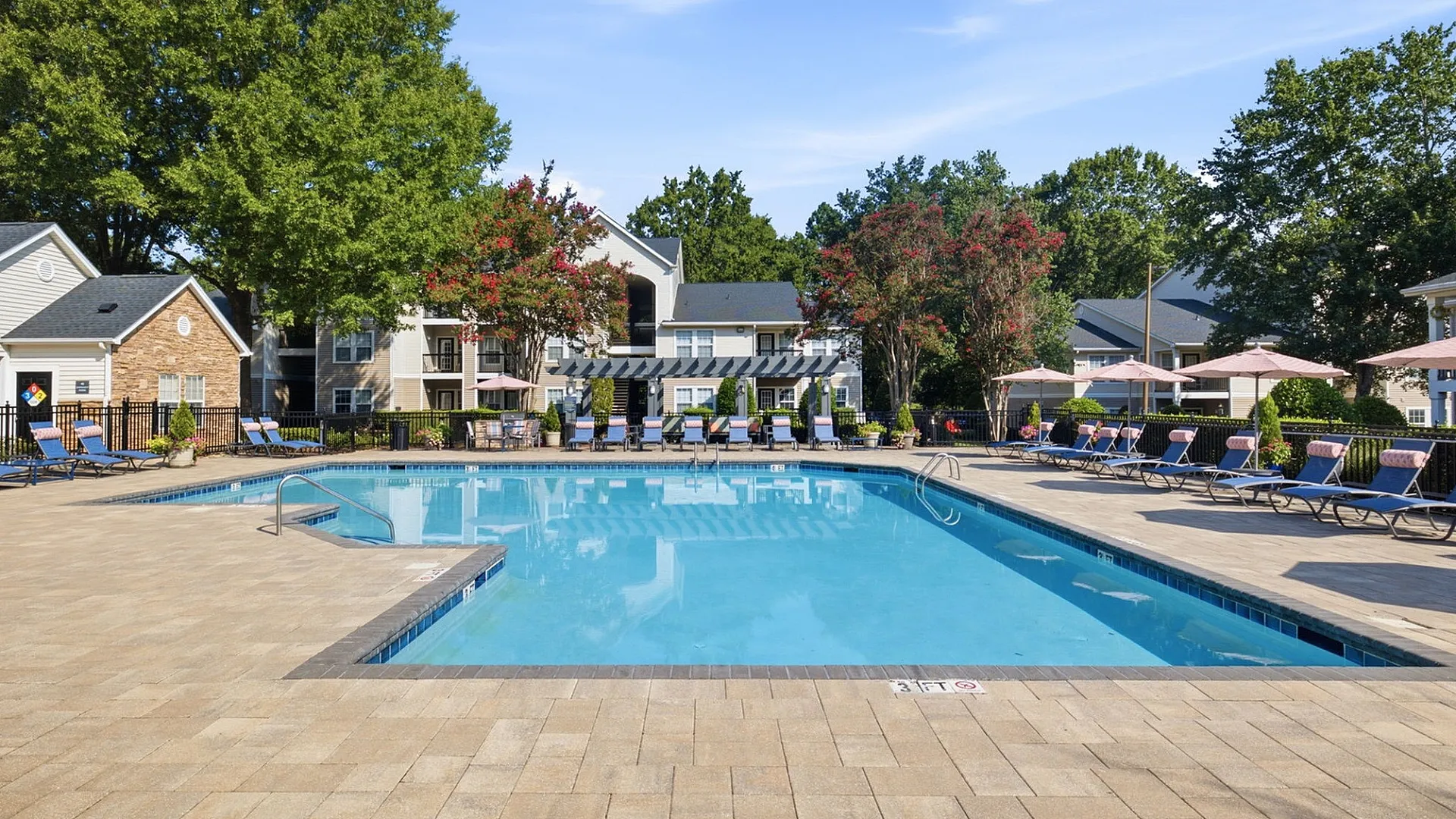 Inviting outdoor pool area with comfortable lounge chairs, surrounded by lush greenery and charming residential buildings.