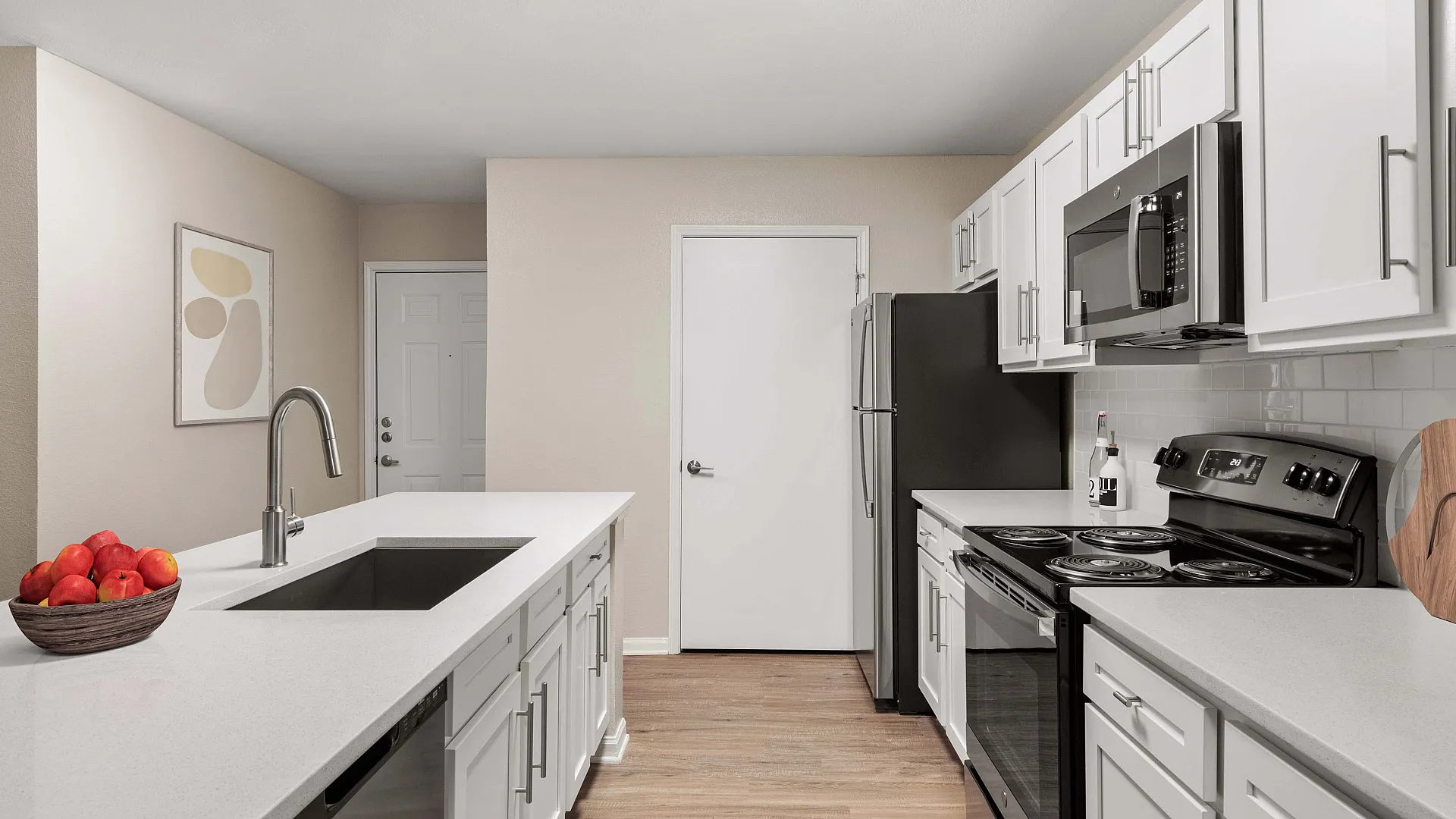 Modern kitchen with sleek white cabinetry, stainless steel appliances, and a stylish white island with an integrated sink and decorative fruit bowl.