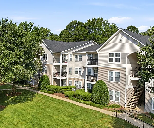 Charming three-story apartment building surrounded by lush greenery and mature trees, featuring private balconies and a serene atmosphere.