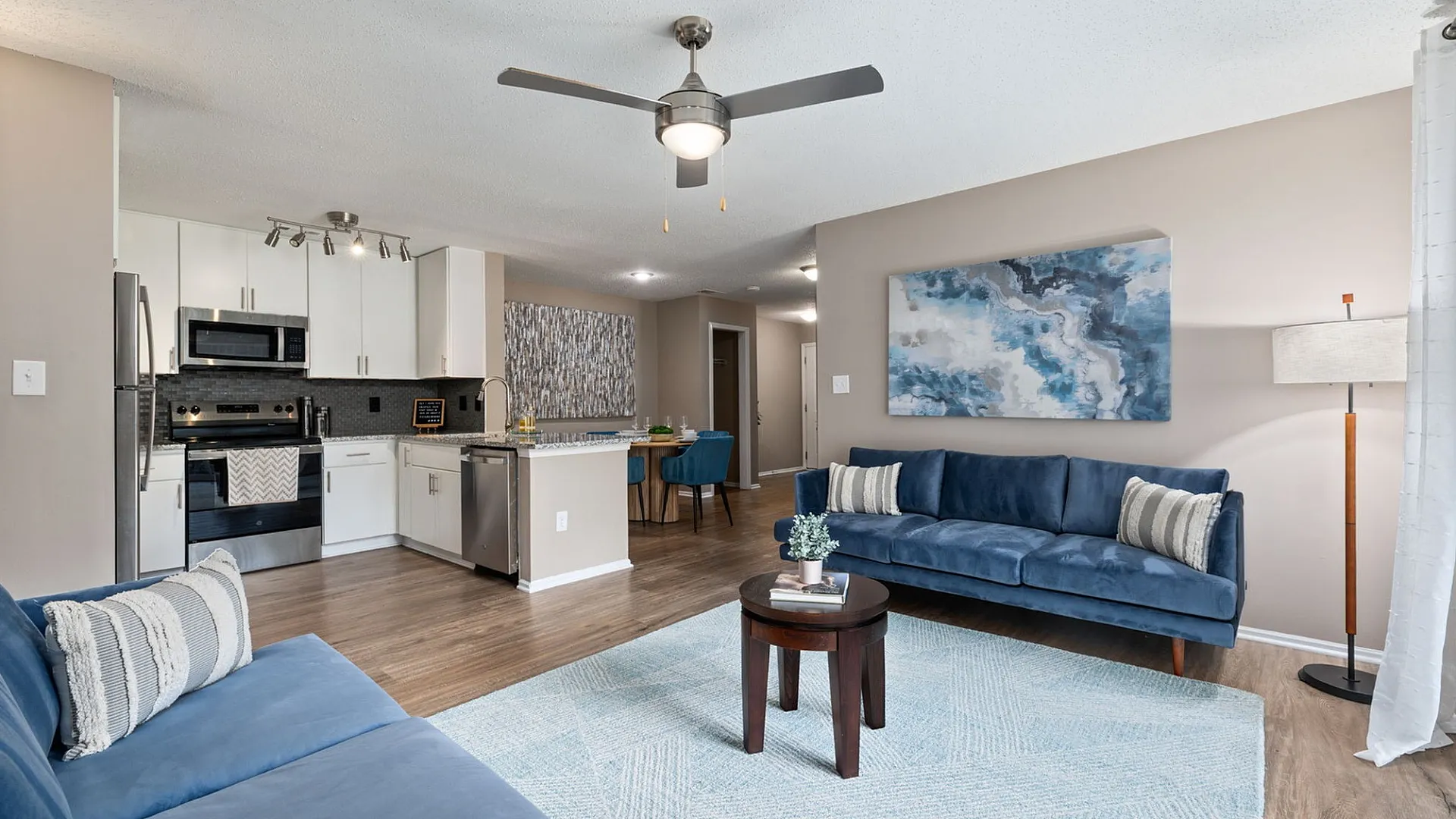 Modern open-concept living space with elegant blue sofas, sleek kitchen with stainless steel appliances, and stylish artwork for a chic and inviting atmosphere.