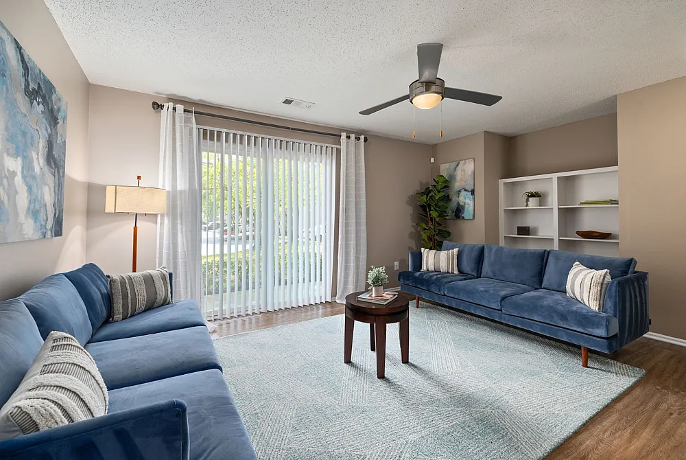 Bright and modern living room featuring sleek blue sofas, a cozy rug, and large windows with elegant curtains for natural light.